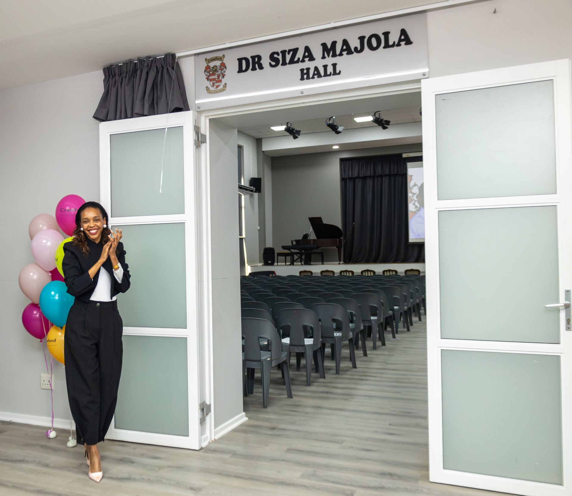 A woman is standing in front of a door that says dr siza majola hall.