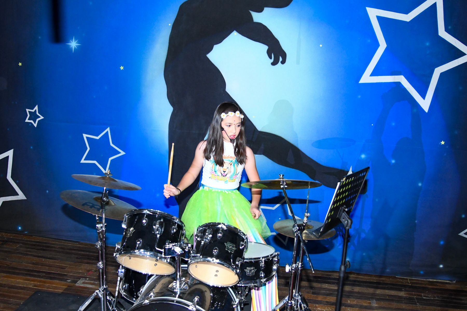 A little girl in a green dress is playing drums