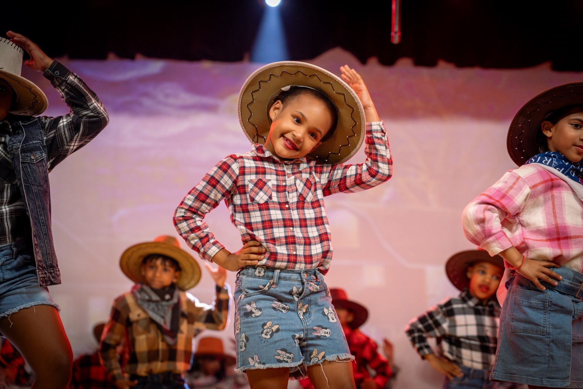 A group of children dressed in cowboy hats and plaid shirts are dancing on a stage.