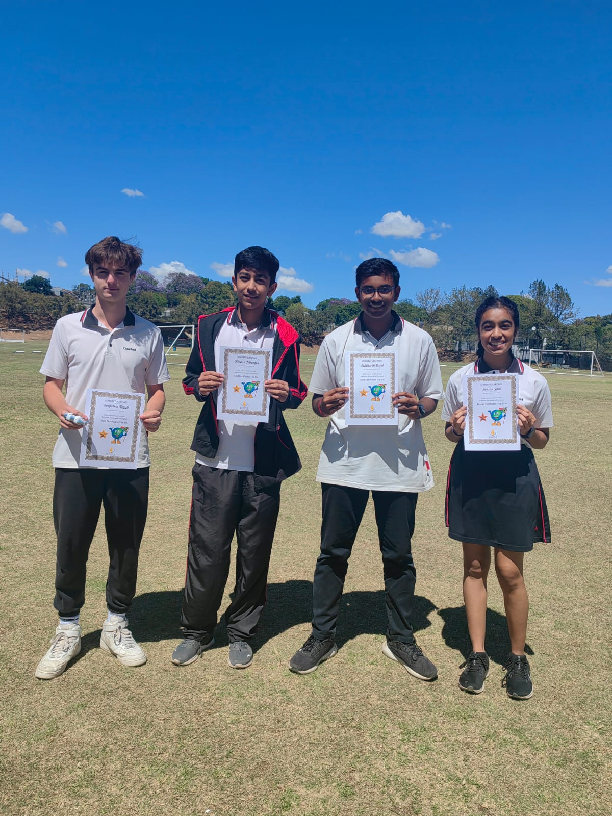 A group of young people are standing in a field holding certificates.