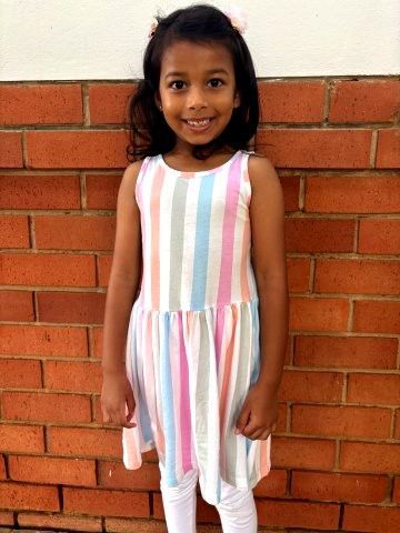 Girl in striped dress stands by brick wall.