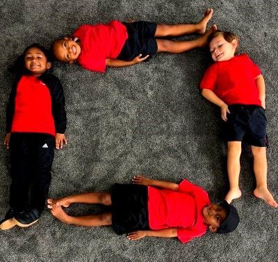 Four children wearing red and black clothing arranged in a square shape on a gray carpet.