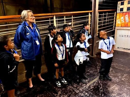 Group of children and an adult looking upward in a museum or similar setting.