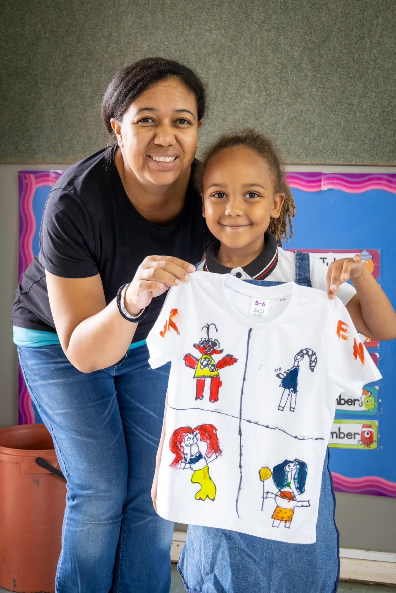 A woman and a little girl are holding a t-shirt with drawings on it.
