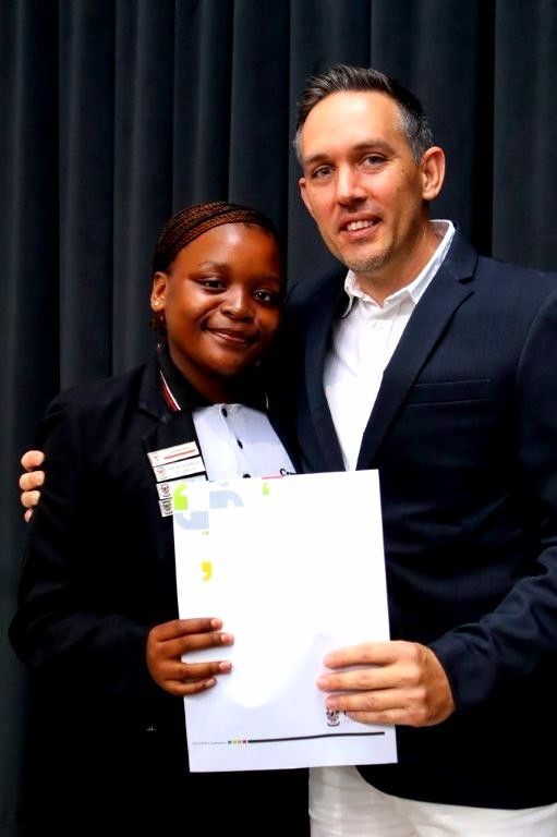 Person in suit poses with a person holding a certificate.  They both smile. Backdrop is dark.