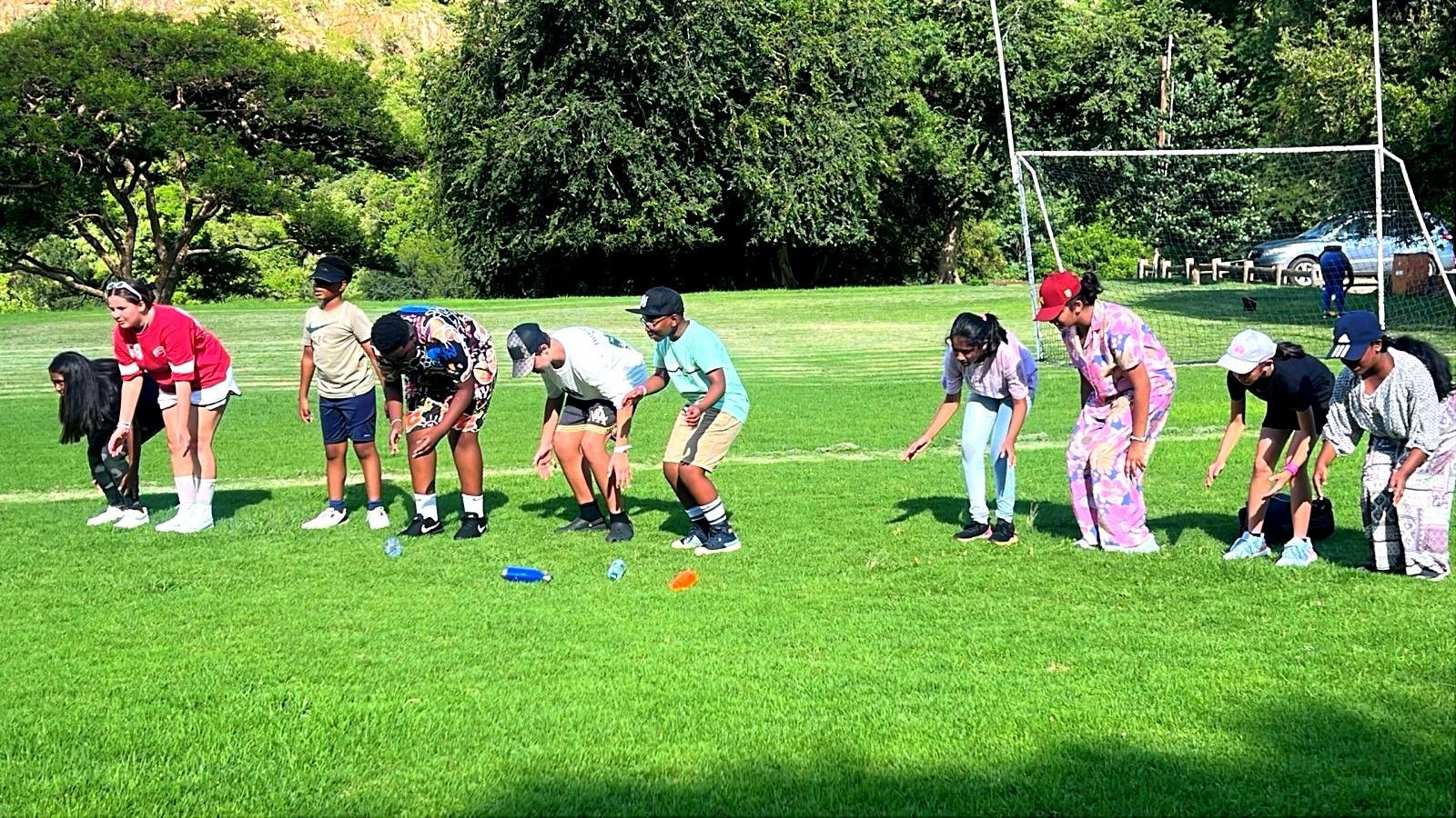 People on a grassy field participating in an outdoor activity, bending down to the ground.