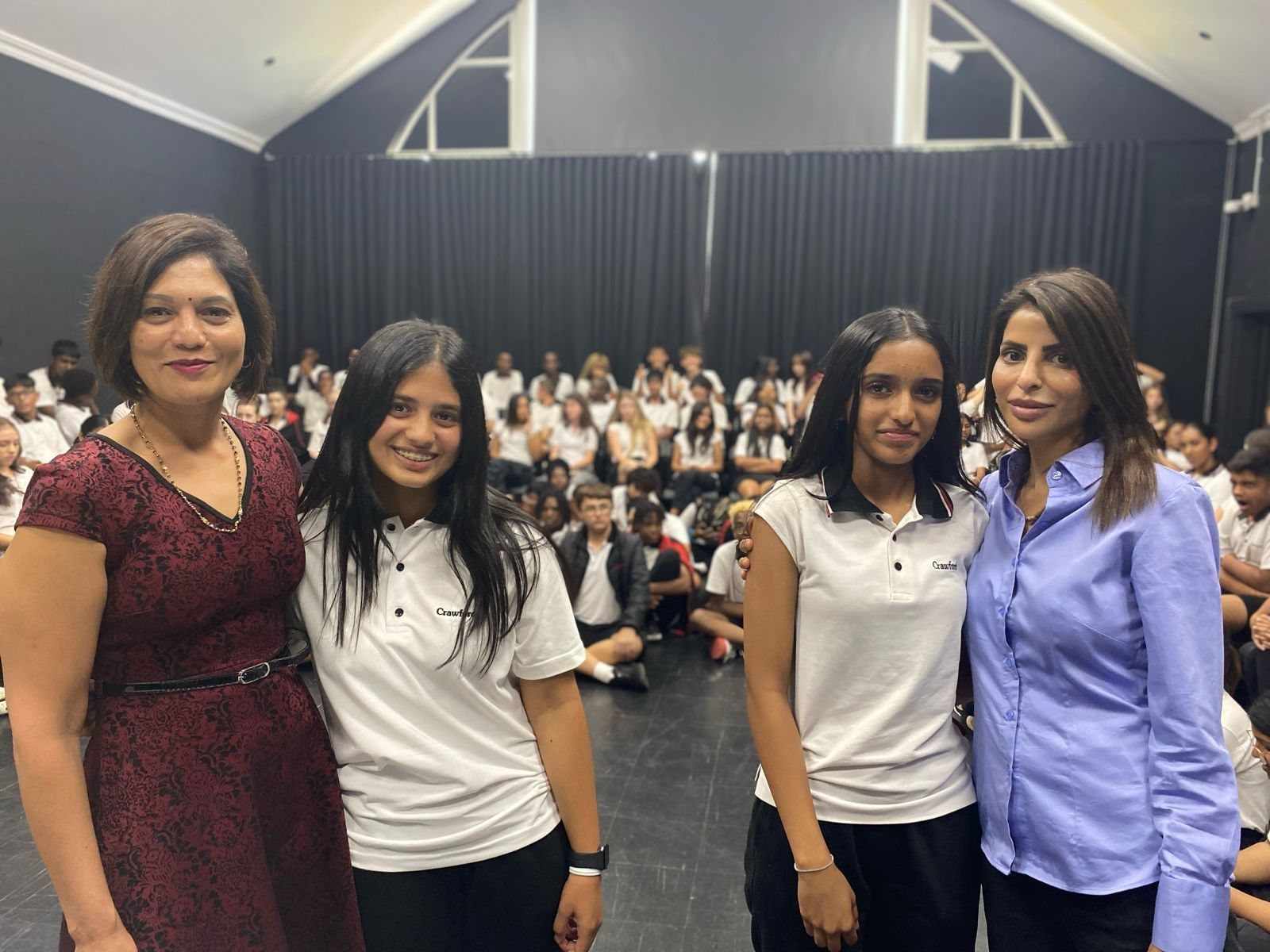 Four women are posing for a picture in front of a crowd of people.