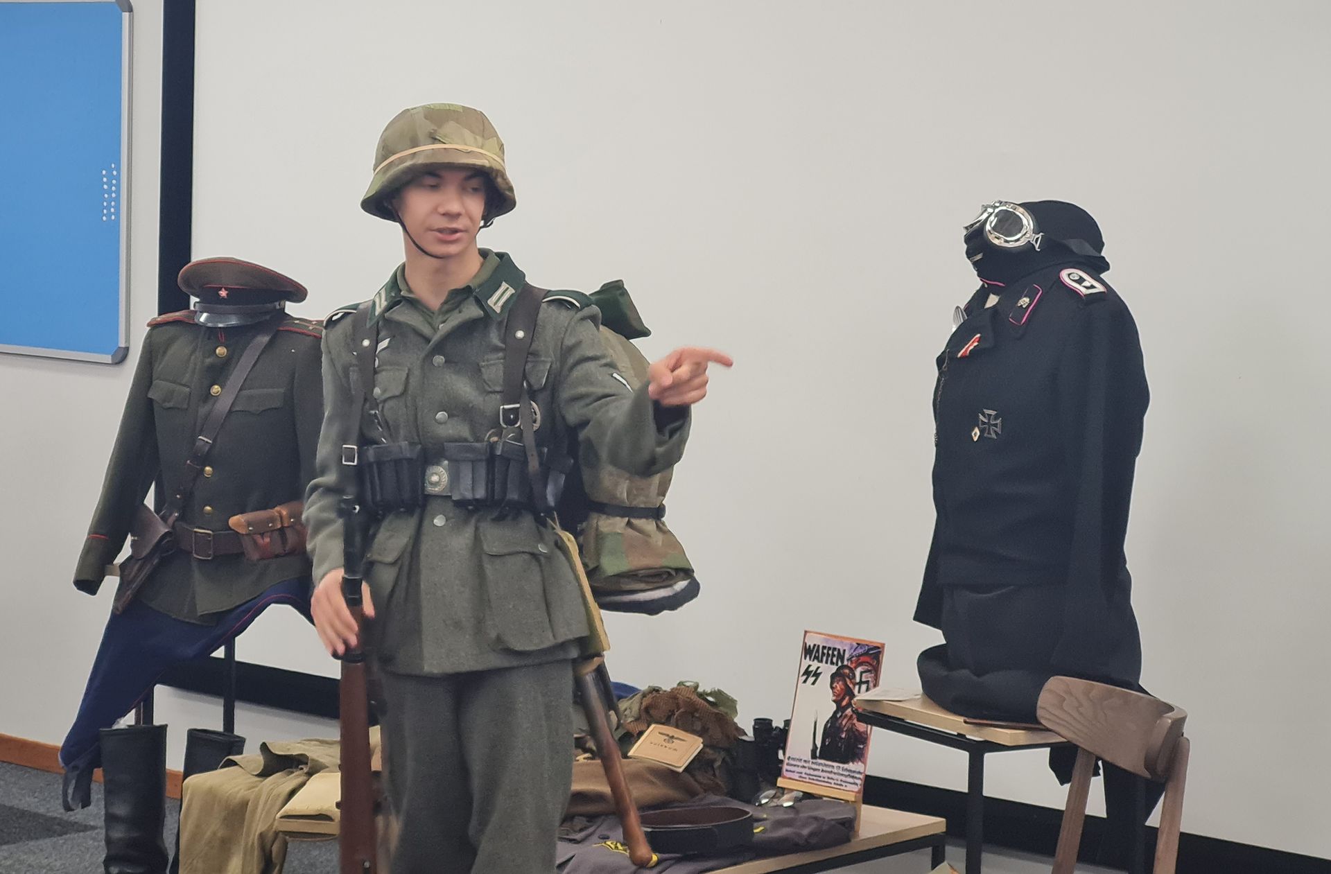 A man in a military uniform is standing in front of a display of military uniforms.