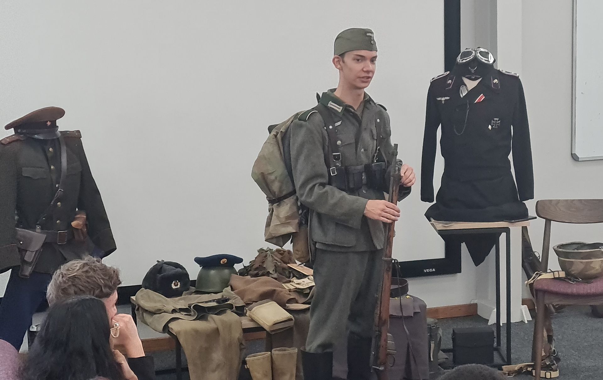 A man in a military uniform is standing in front of a group of people.