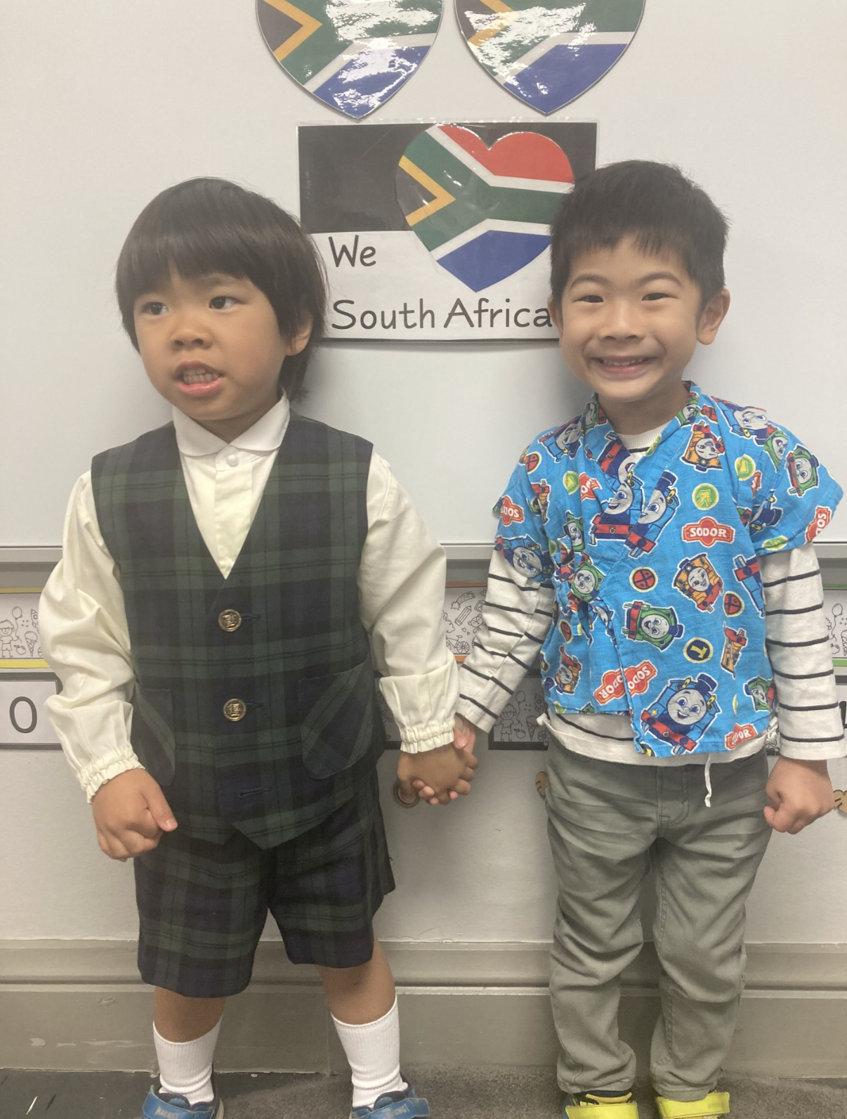 Two young boys are holding hands in front of a sign that says south africa