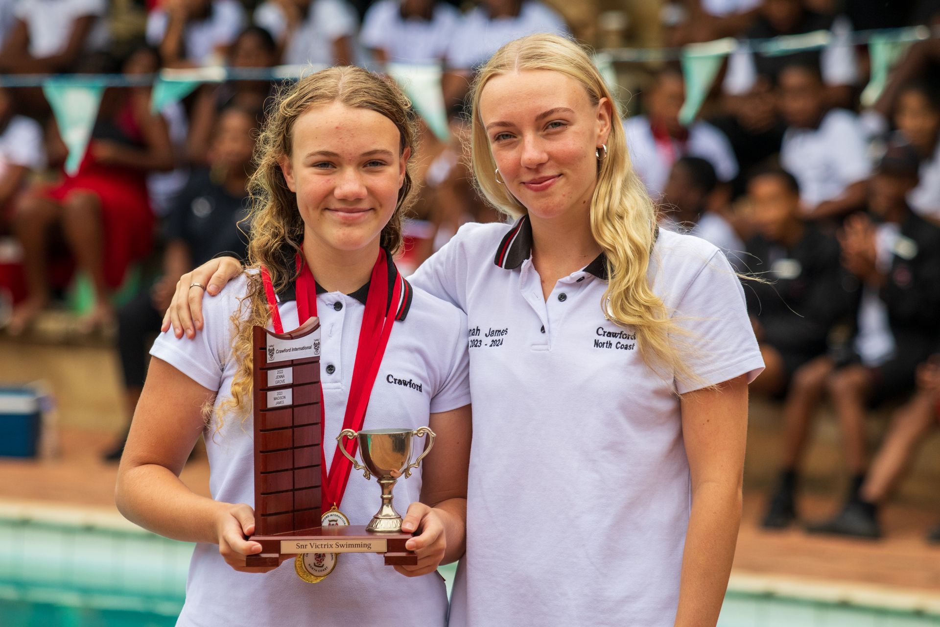 Two young women are standing next to each other holding a trophy.