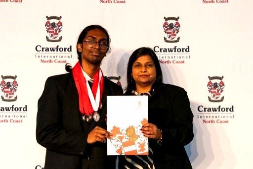 Two people posing with a certificate and medals in front of a school banner.