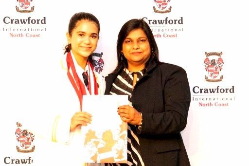 A young person in a school uniform receives a certificate, standing beside a woman at a Crawford school event.
