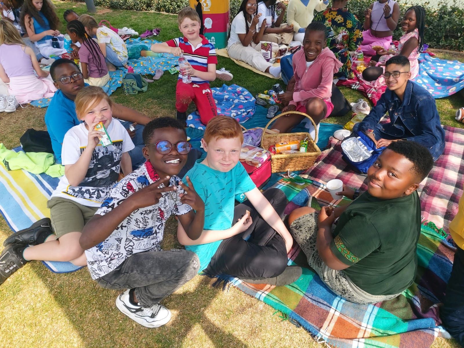 A group of children are sitting on blankets in the grass having a picnic.
