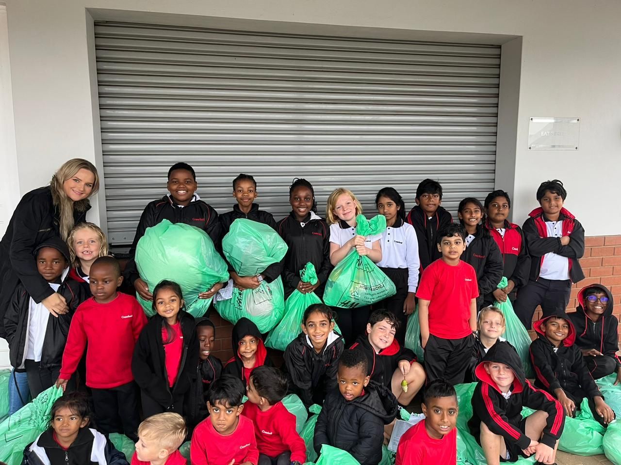 A group of children are posing for a picture while holding green bags.