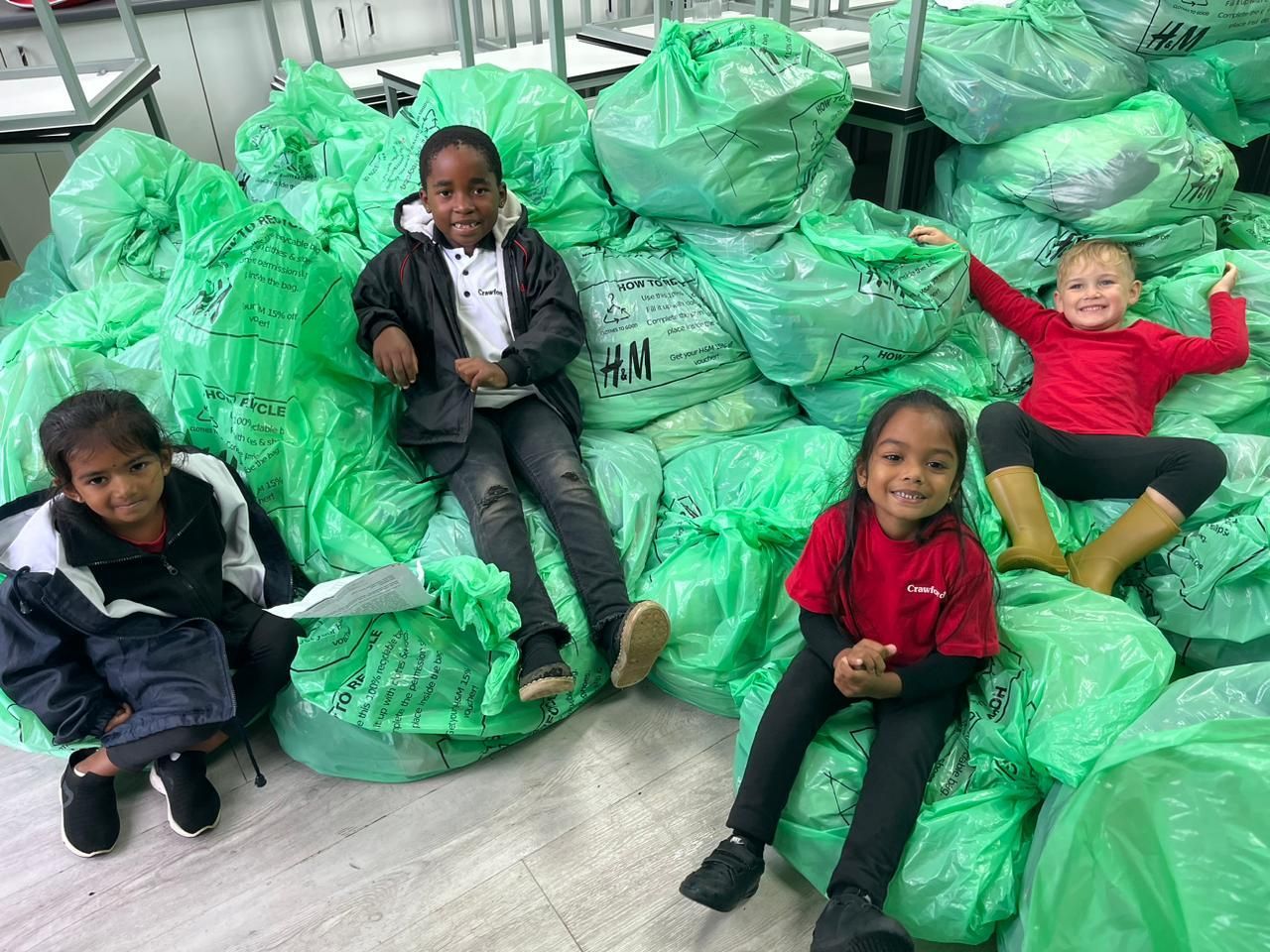 A group of children are sitting on a pile of green bags.