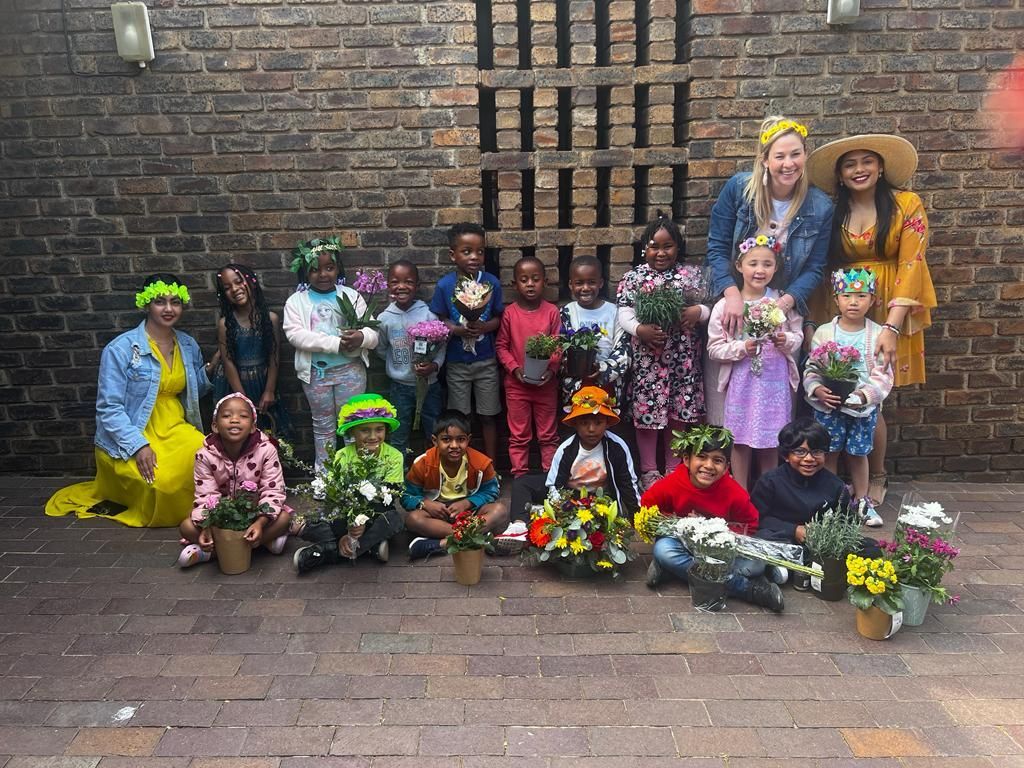 A group of children are posing for a picture with flowers in front of a brick wall.
