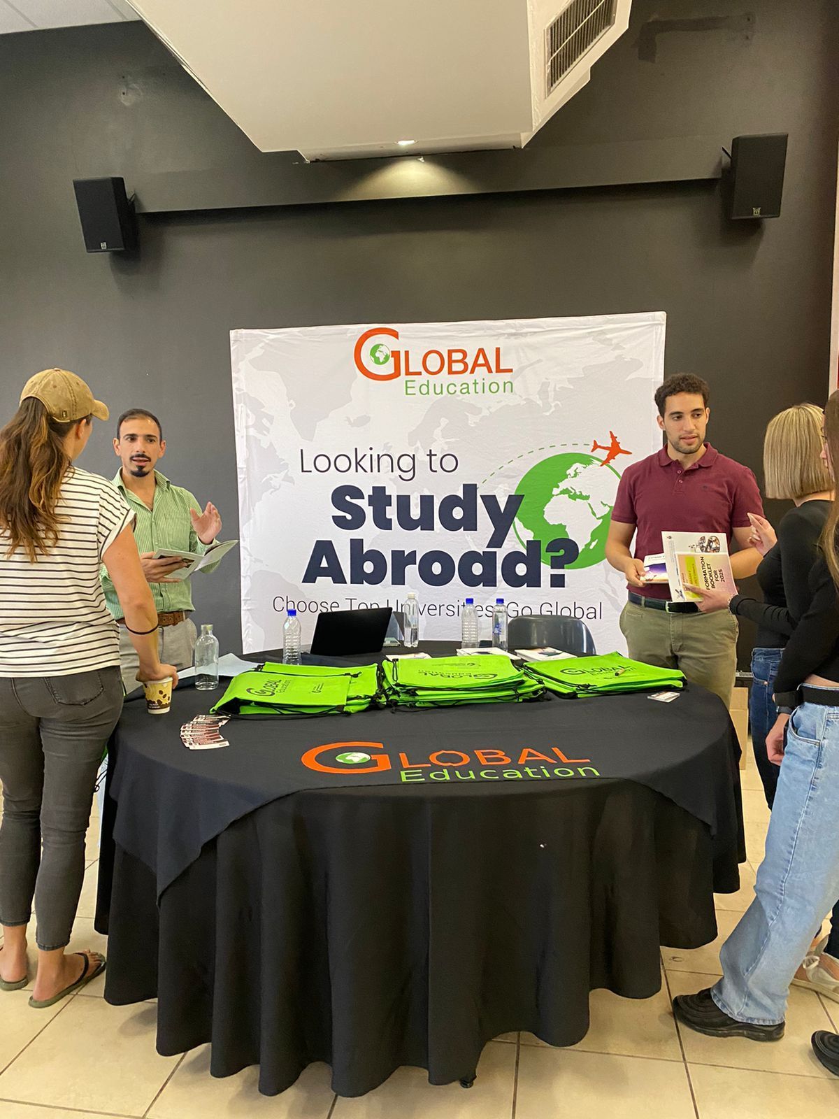 A group of people are standing around a table with a sign that says `` looking to study abroad ''.