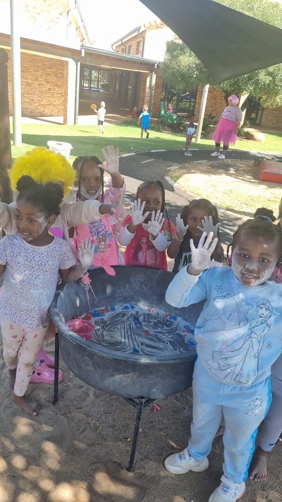 A group of children are standing around a large bowl of soap bubbles.
