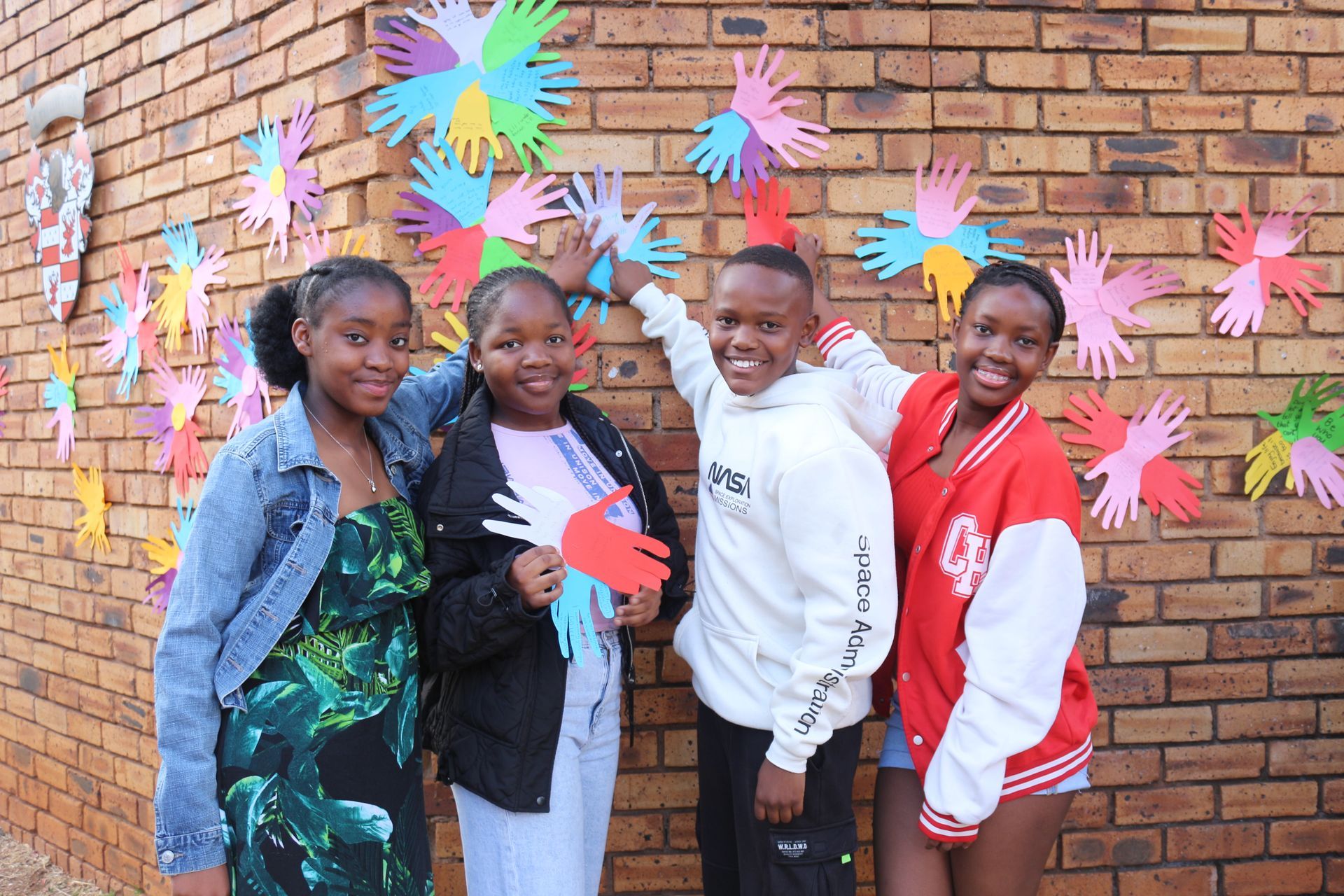 A group of young girls are standing in front of a brick wall with paper hands on it.