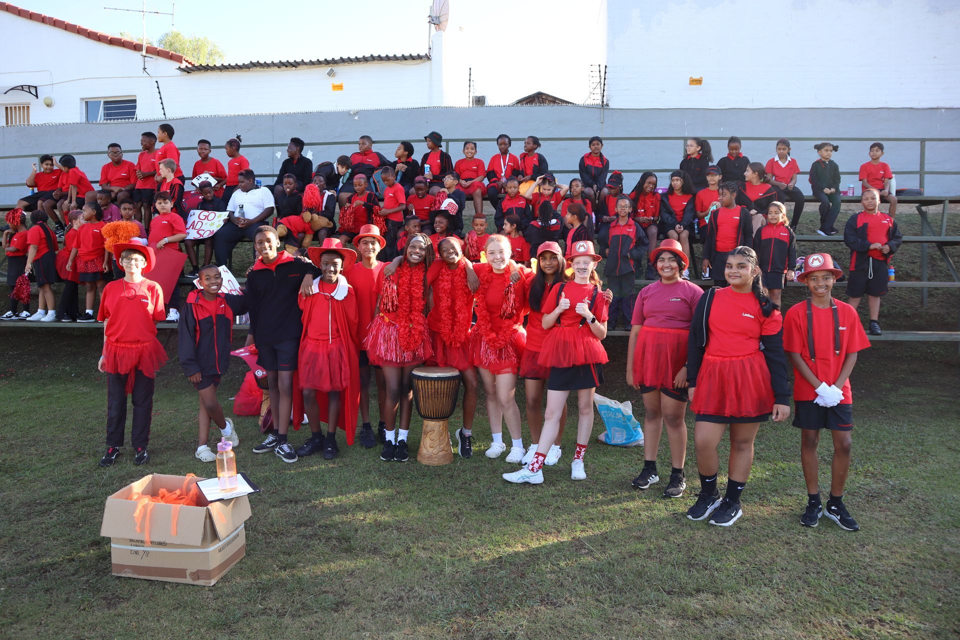 A large group of children dressed in red are standing in a field.