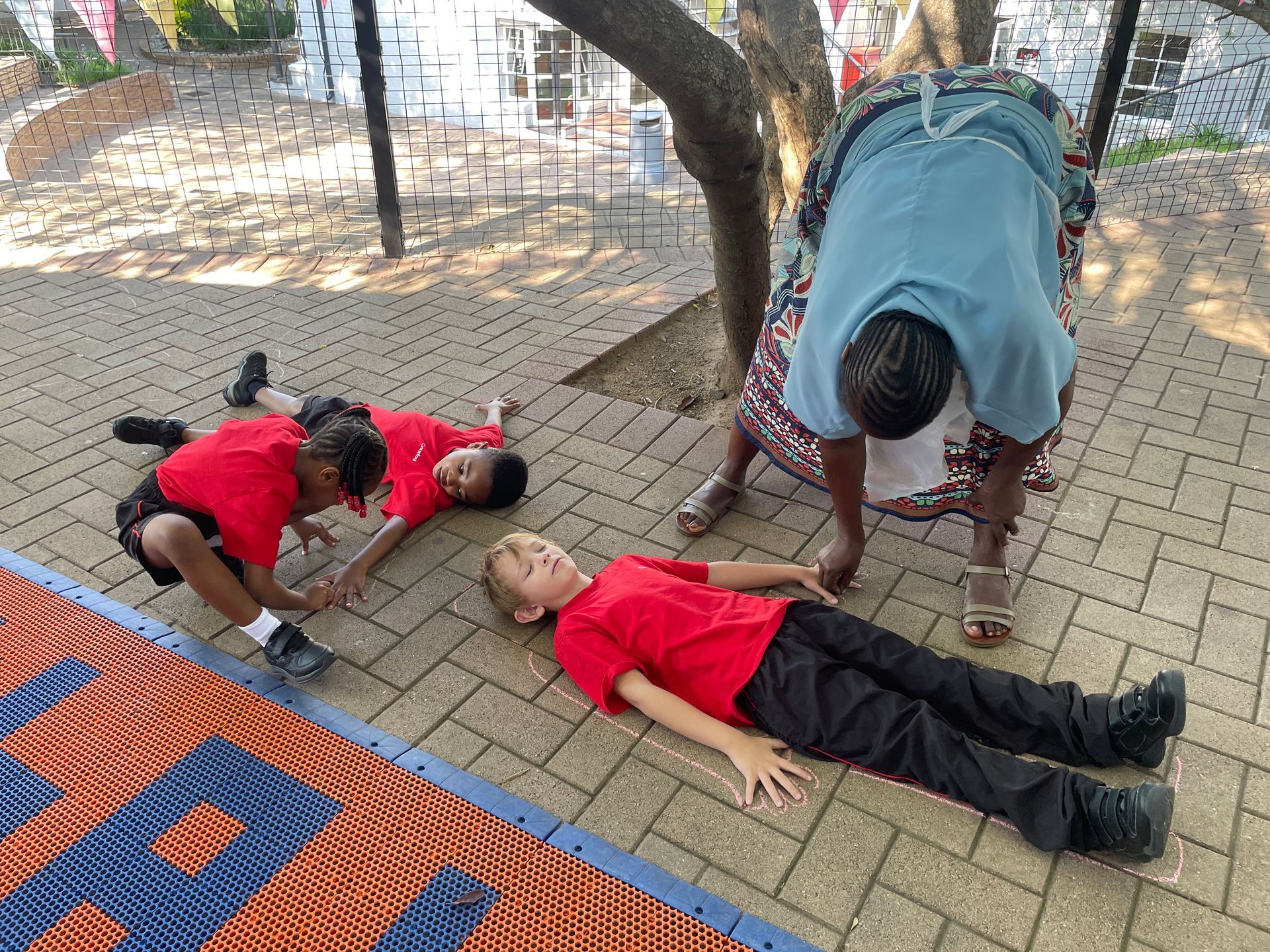 A group of children are laying on the ground under a tree.