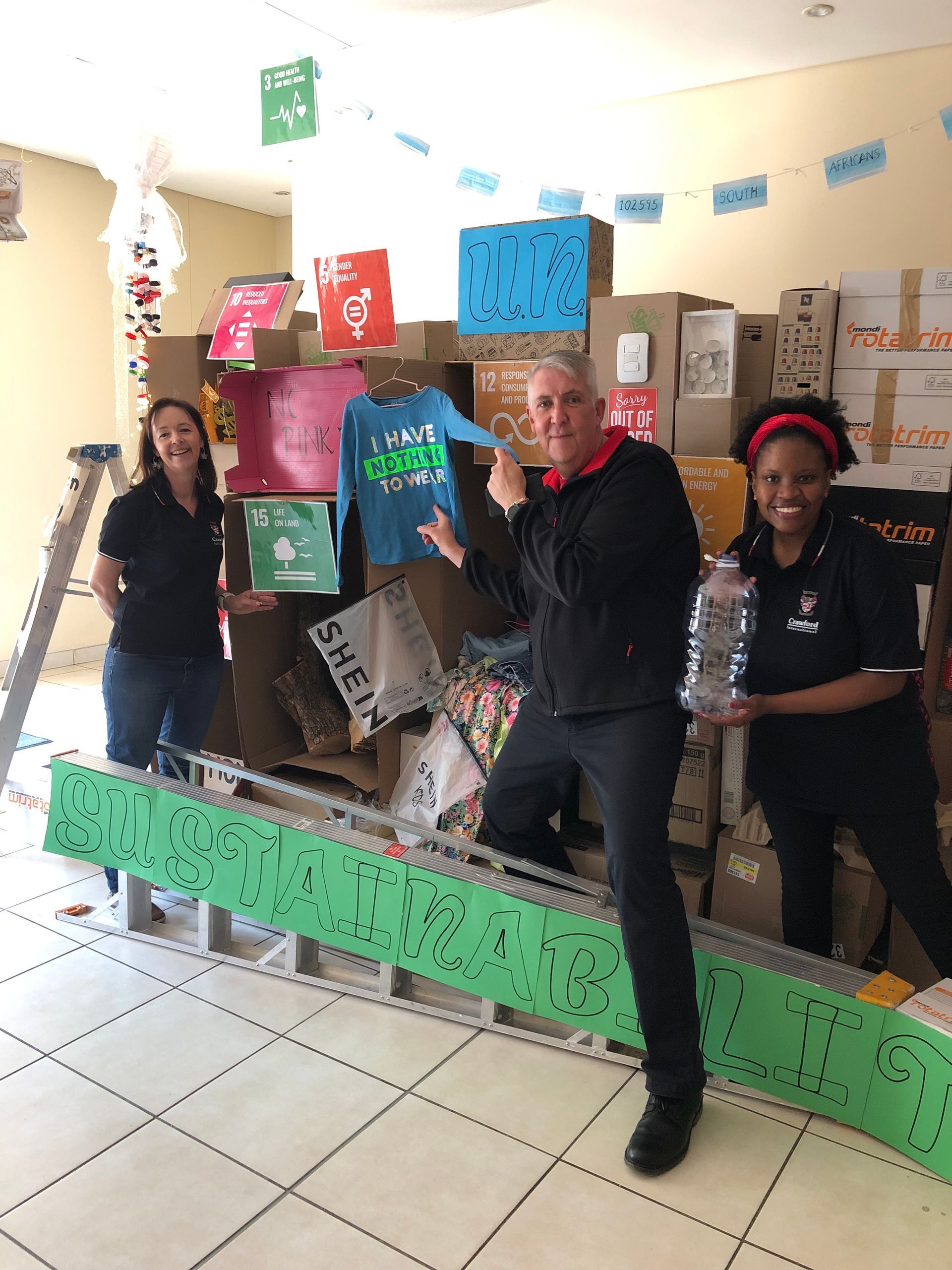 A man and two women are standing in front of a pile of boxes.