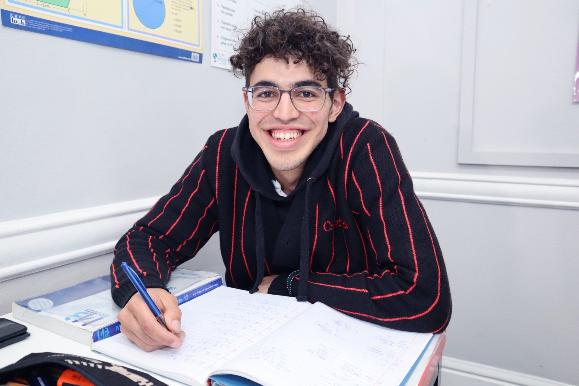 a young man is sitting at a desk in a classroom writing in a notebook .