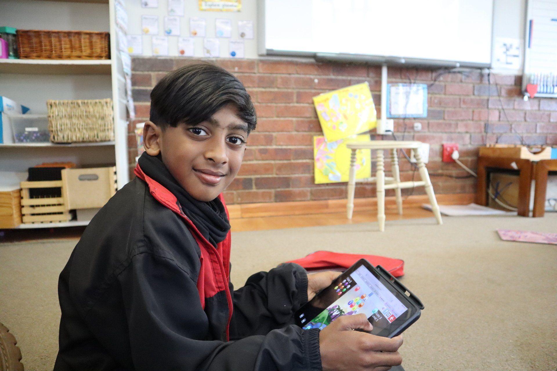 a young boy is sitting on the floor in a classroom holding a tablet computer .