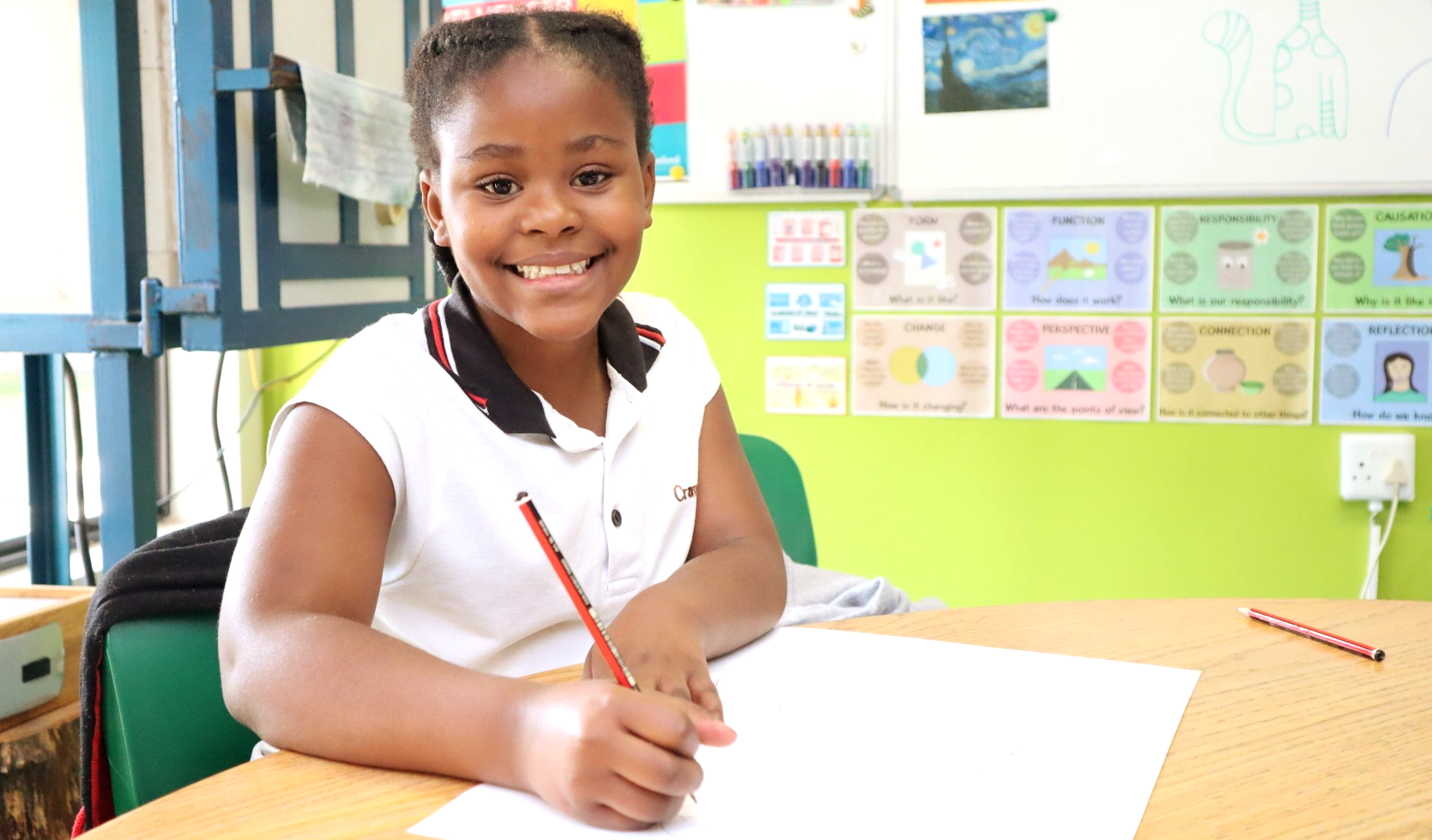 a young girl is sitting at a desk in a classroom with a pencil in her hand .