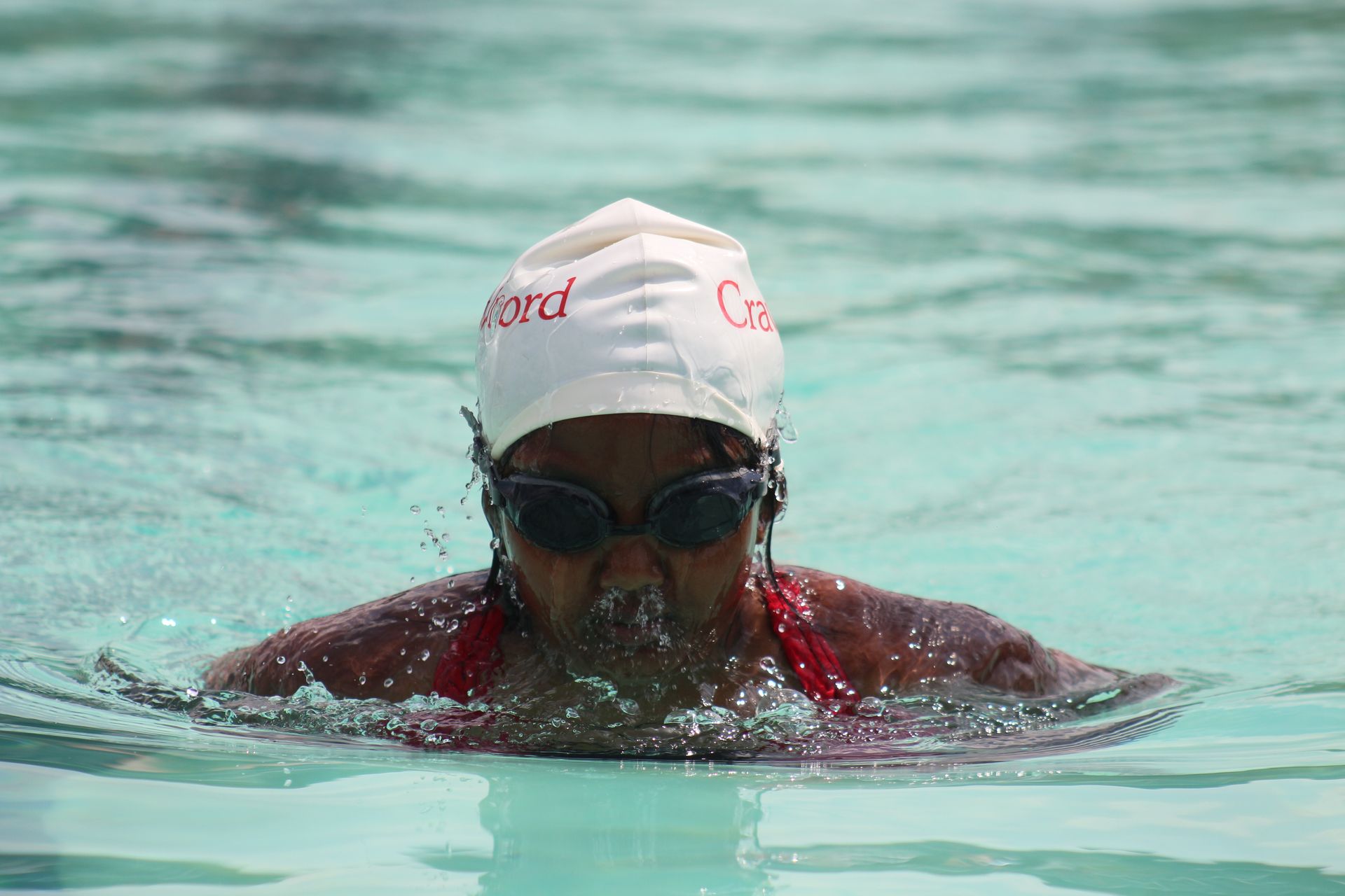 A woman wearing a swim cap and goggles is swimming in a pool.
