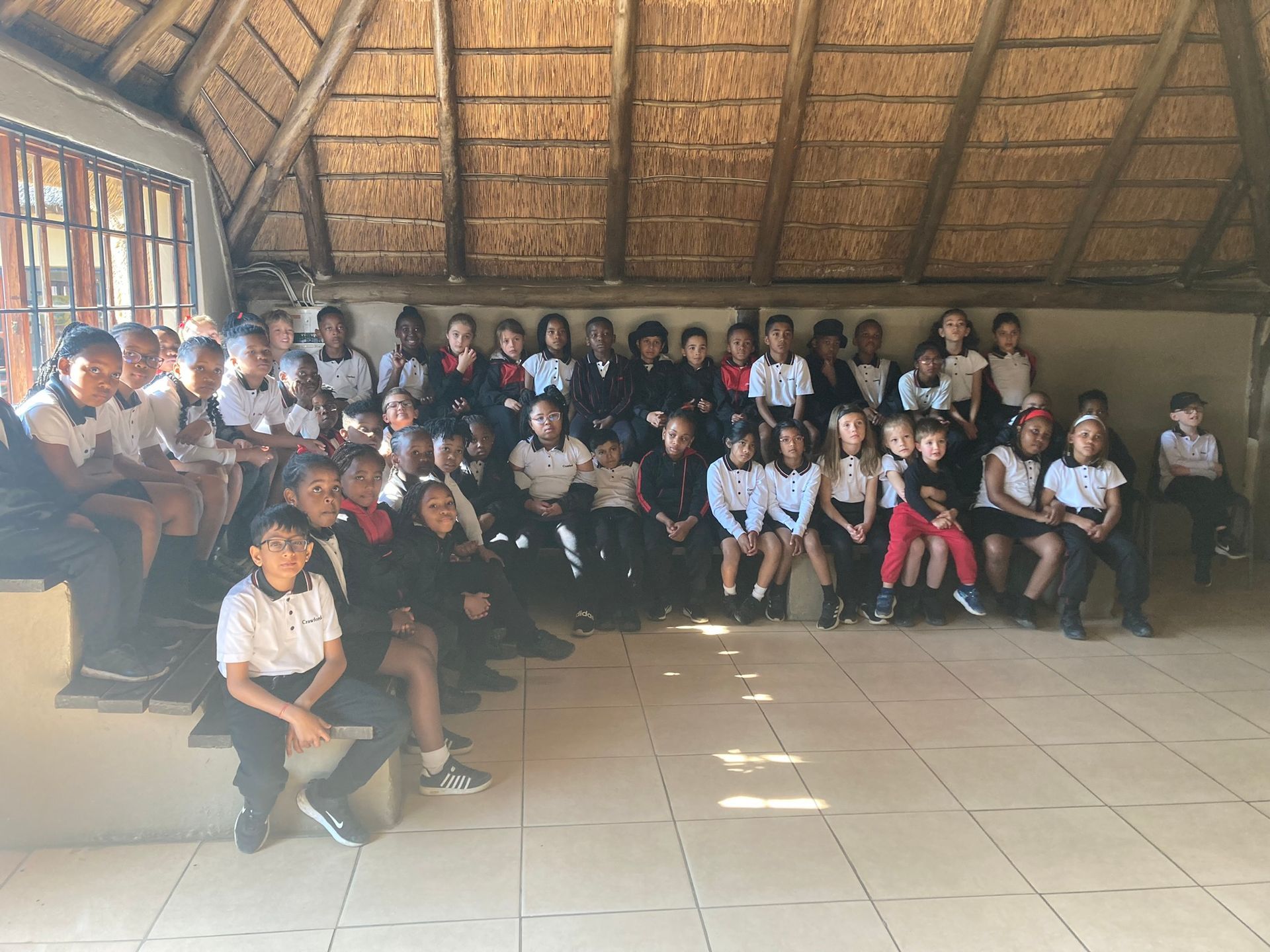 A group of children are posing for a picture in a room with a thatched roof.