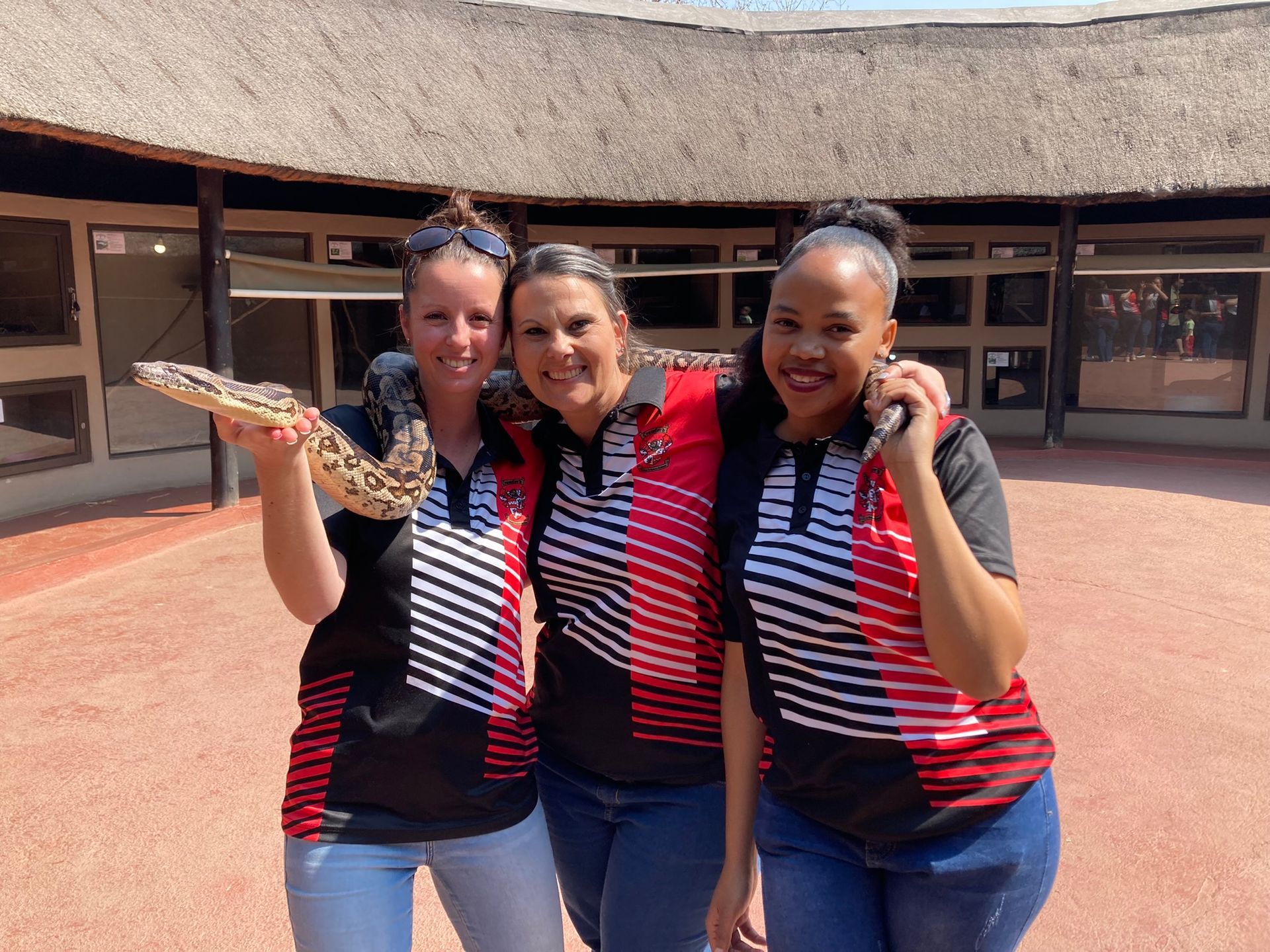 Three women are posing for a picture while one of them is holding a snake.