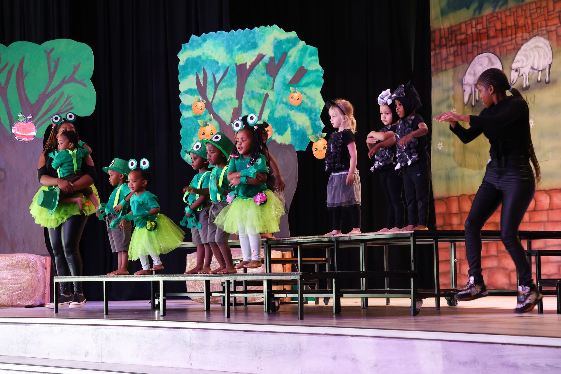 A group of children are standing on a stage in front of a tree.