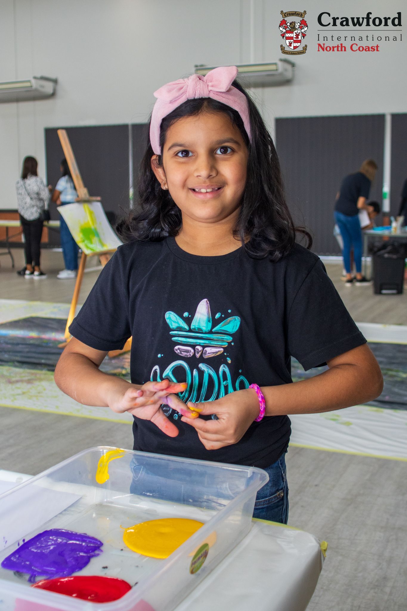 A young girl is standing in front of a table with containers of paint.