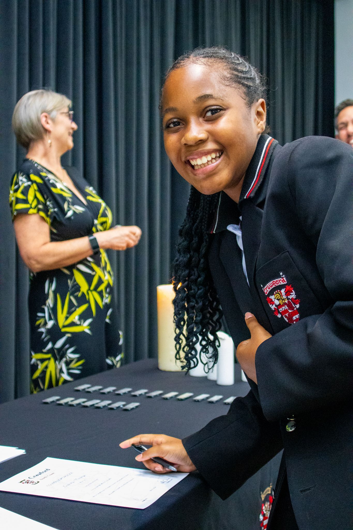 A woman in a black jacket is smiling while standing at a table.