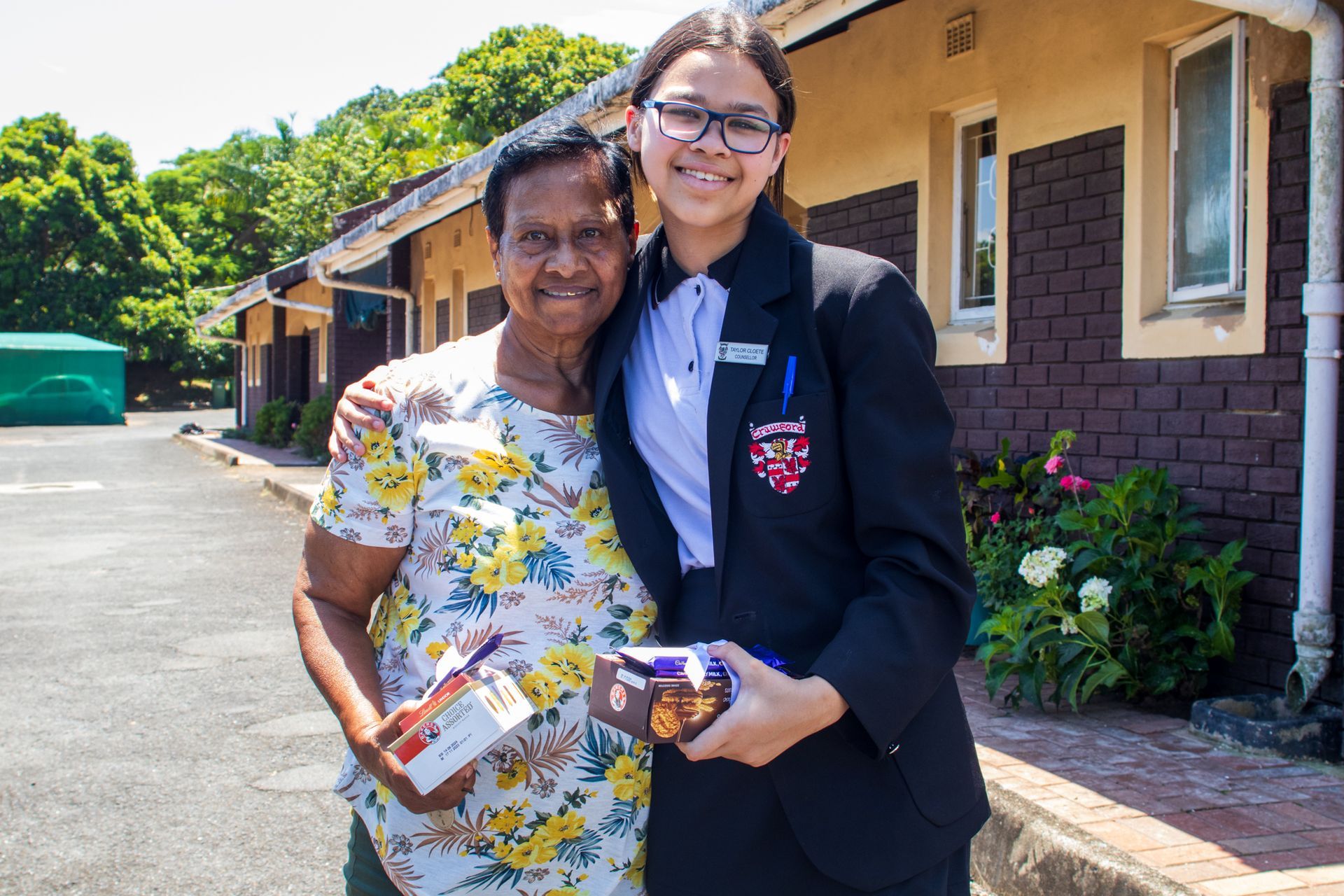 A young girl is standing next to an older woman in front of a brick building.