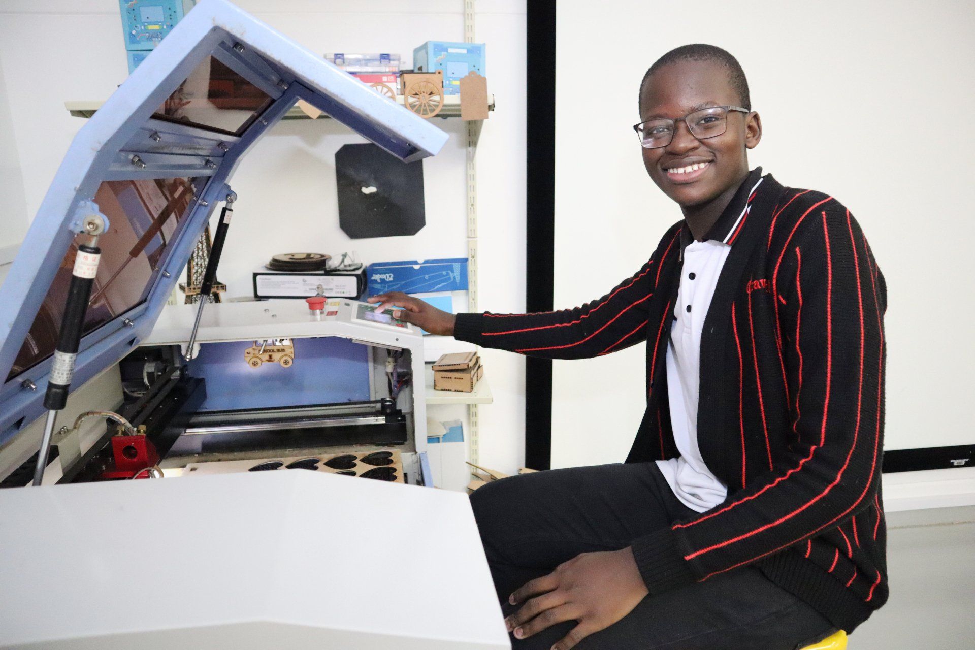 a boy in a striped jacket is sitting in front of laser cutter