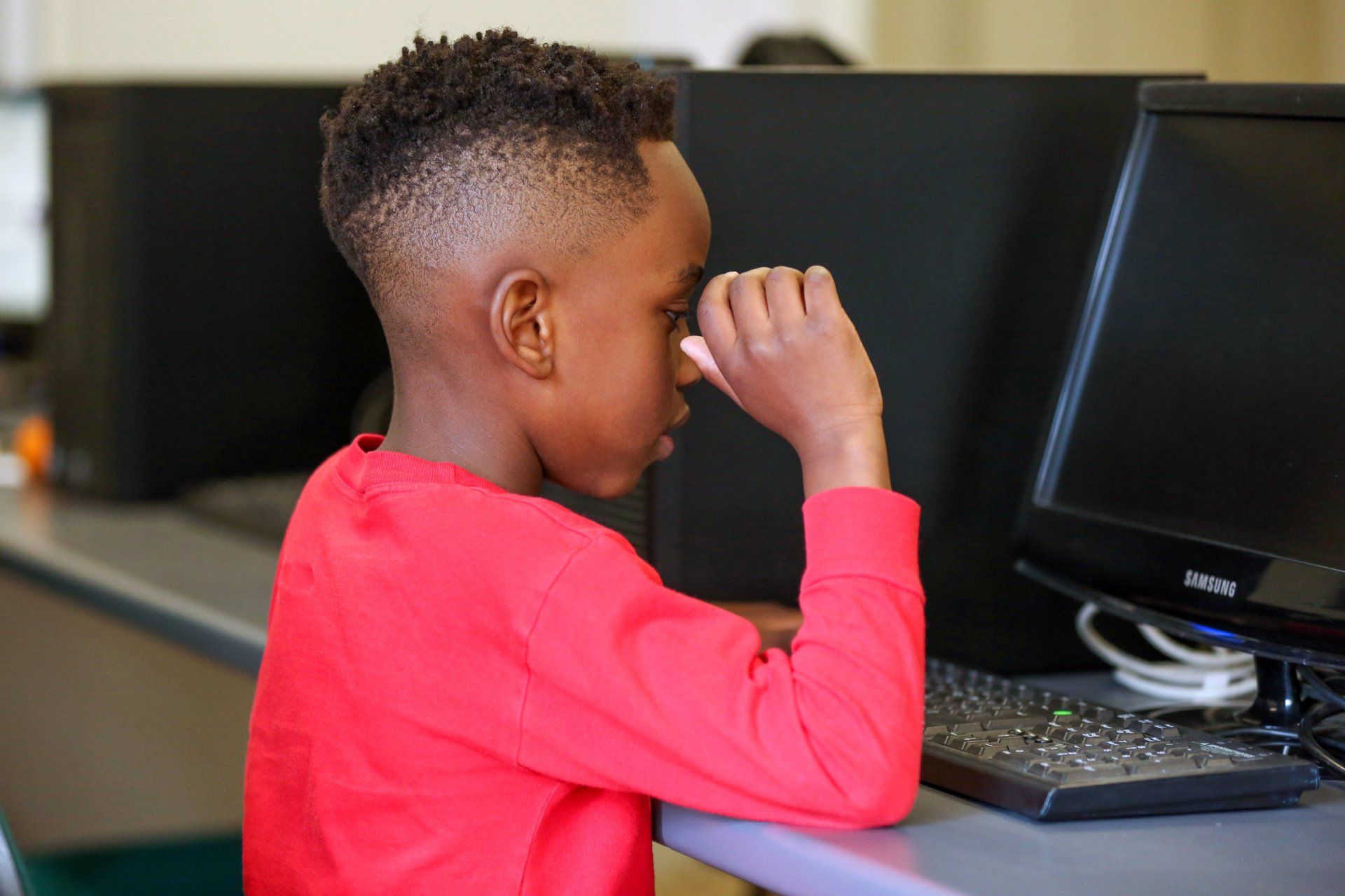 Boy in red shirt at a computer, looking intently at the screen.