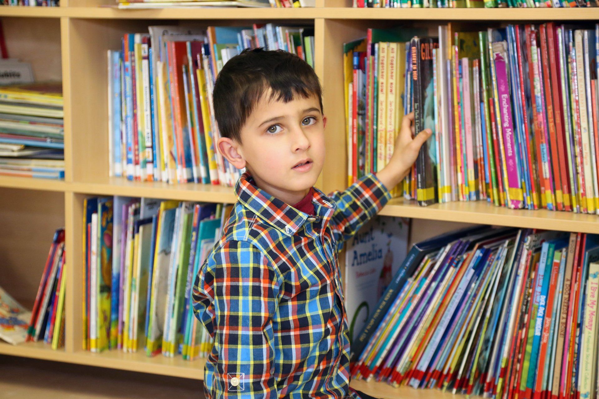 a young boy is looking at books on a bookshelf in a library .
