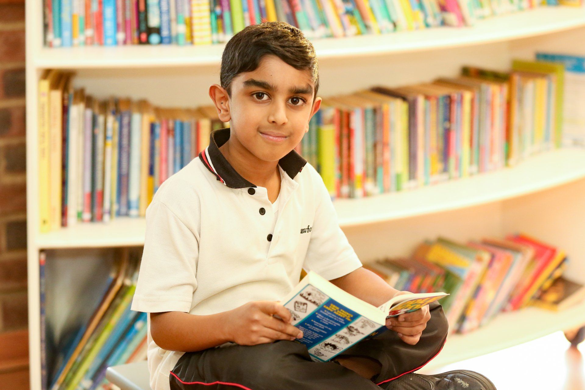 a young boy is sitting in front of a bookshelf reading a book .
