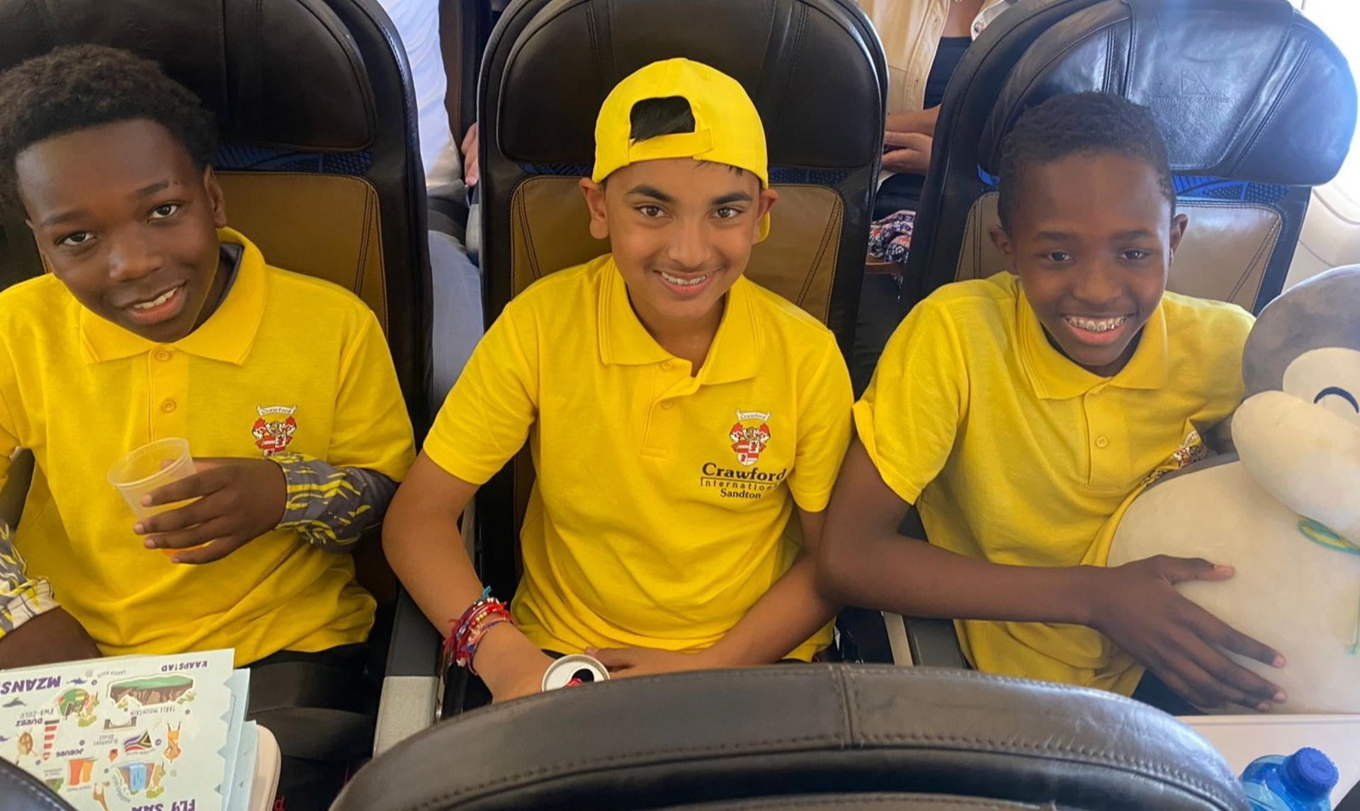 Three young boys in yellow shirts are sitting on an airplane.
