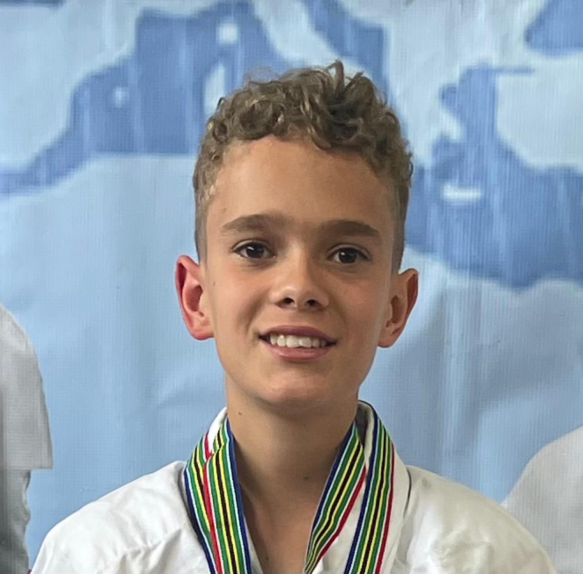 Boy in karate gi with medal smiles, blue background.