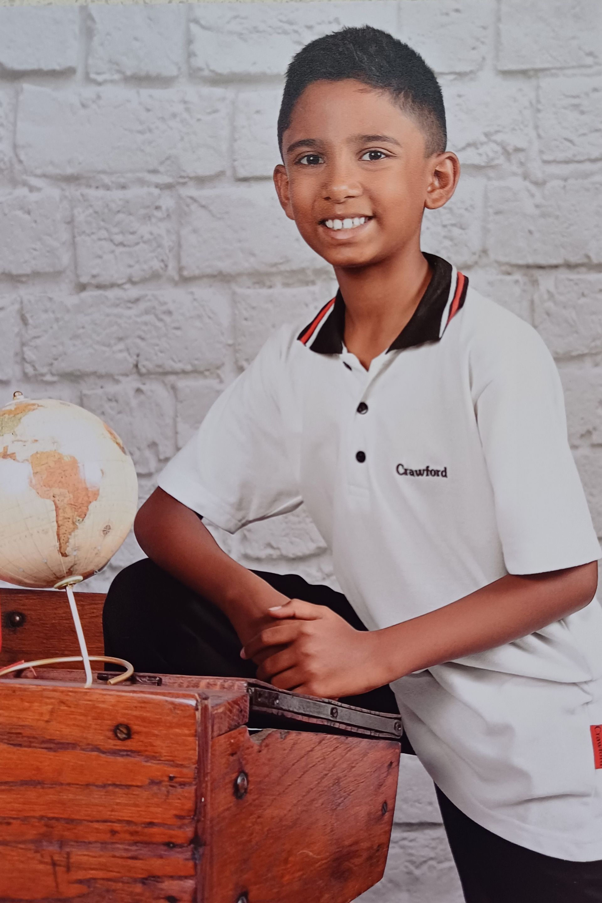 A young boy is sitting on a wooden box next to a globe.