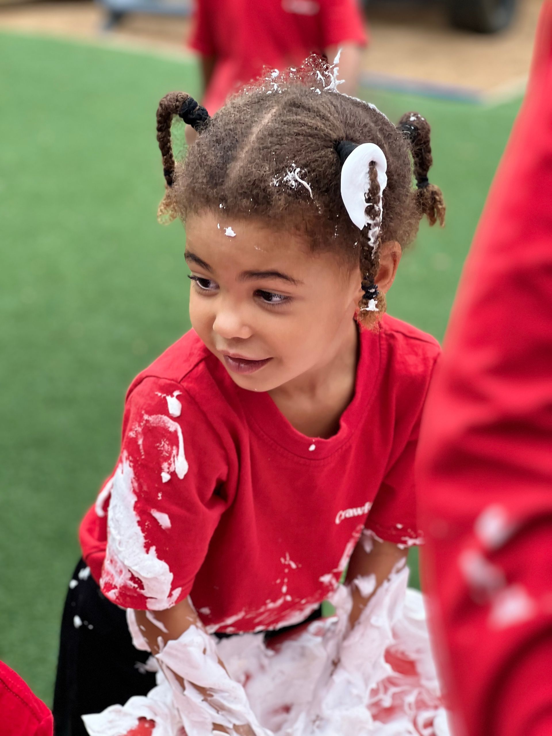 A little girl in a red shirt is covered in white foam