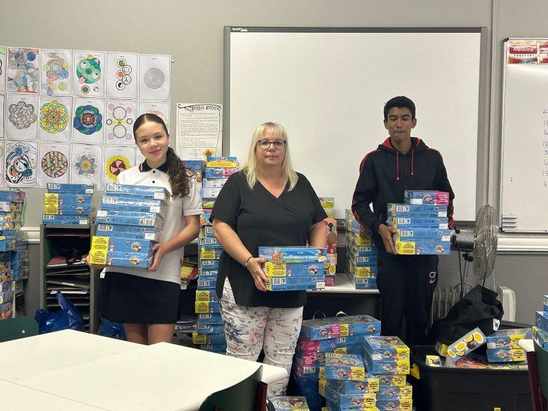 A group of people are standing in a classroom holding boxes.