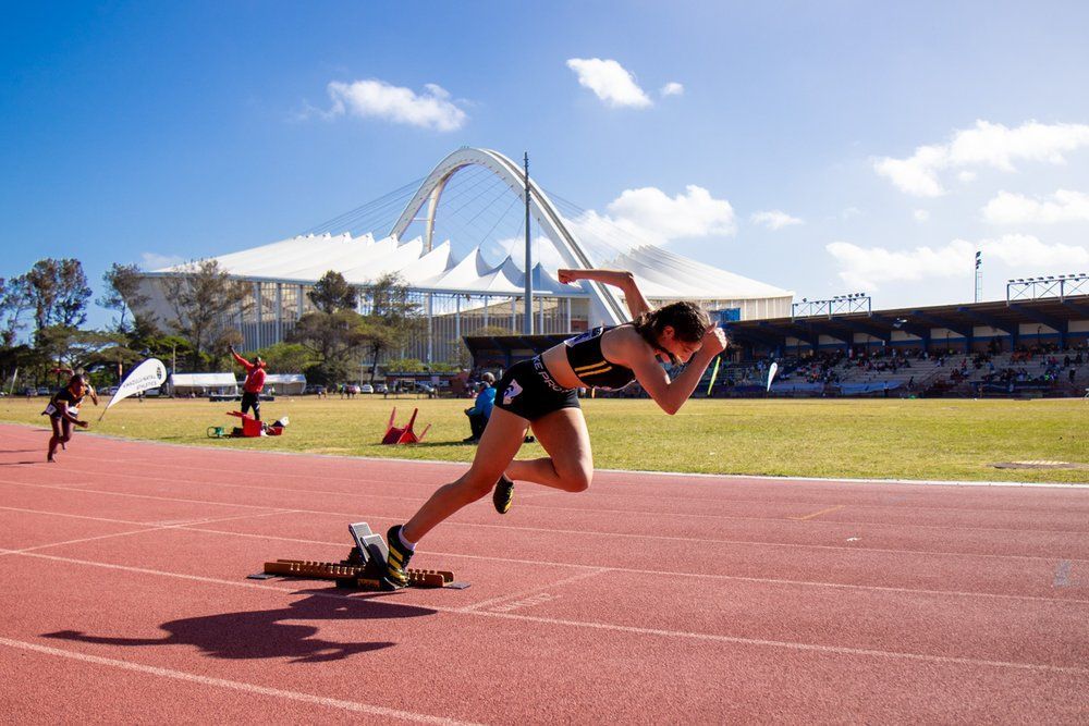 A woman is running on a track with a stadium in the background.