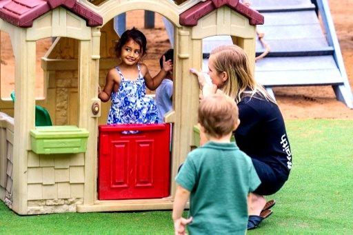 Child in playhouse, another child, and adult interact on grass.
