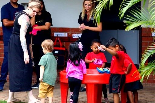 Children playing at a red table with adults nearby outside.