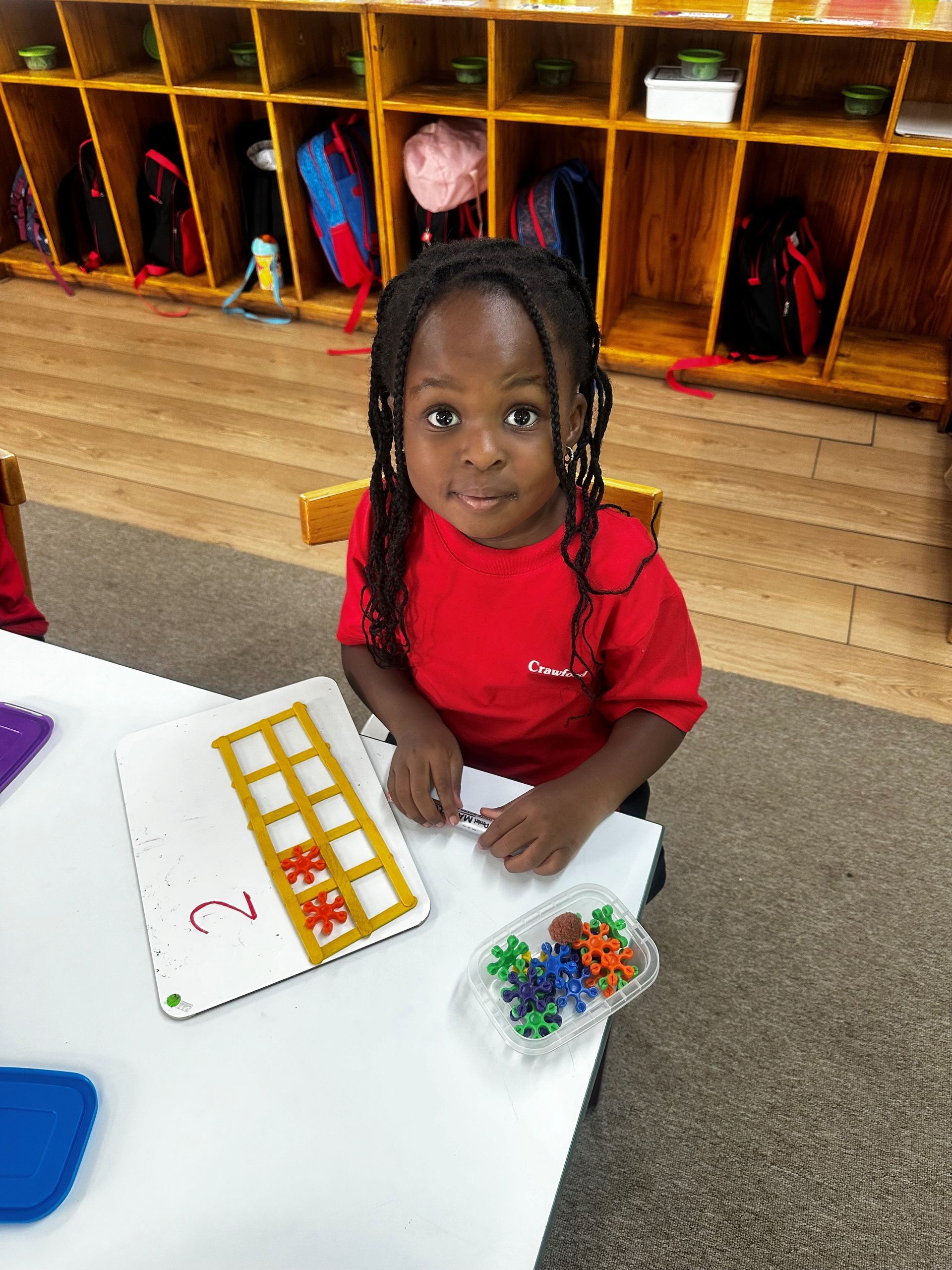 A little girl is sitting at a table in a classroom playing with beads.